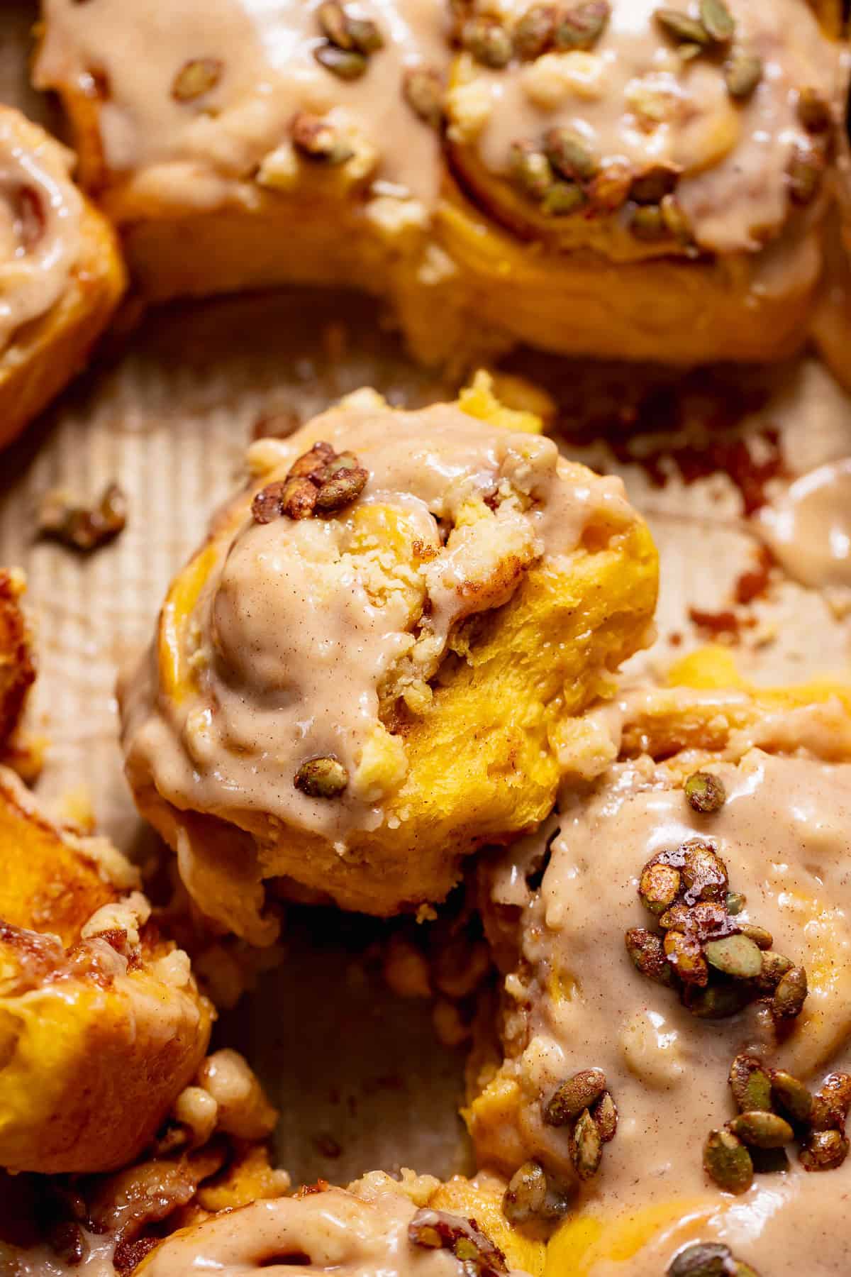 Pumpkin cinnamon rolls with cinnamon cream cheese frosting and candied pumpkin seeds in a baking pan.