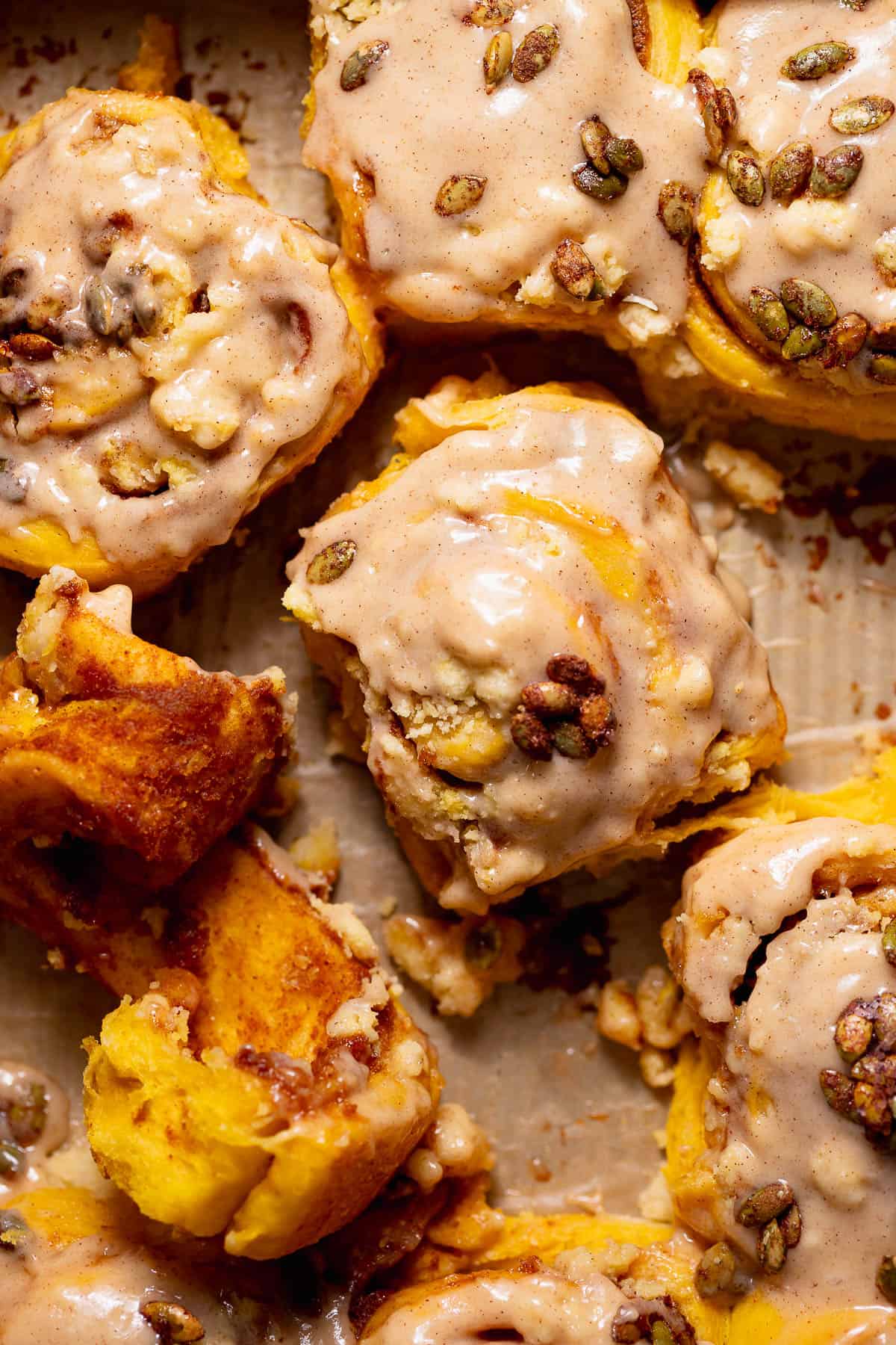 Pumpkin cinnamon rolls with cinnamon cream cheese frosting and candied pumpkin seeds in a baking pan.
