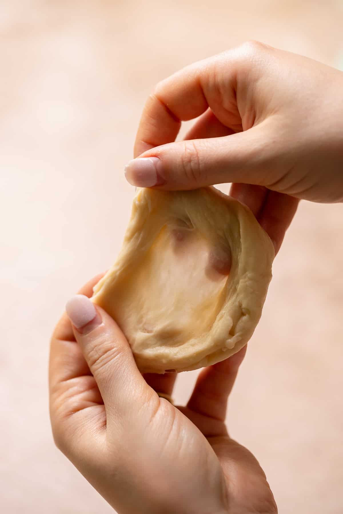 Two hands stretching the donut dough to show the strong gluten windowpane.