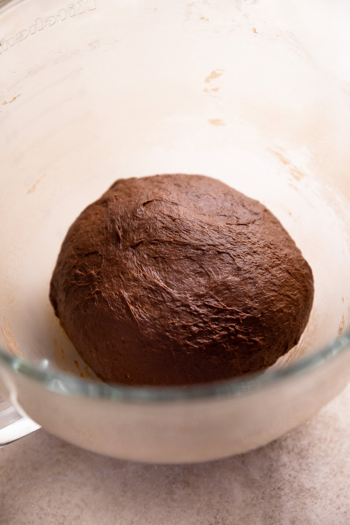 A ball of chocolate yeast dough resting in a glass bowl.
