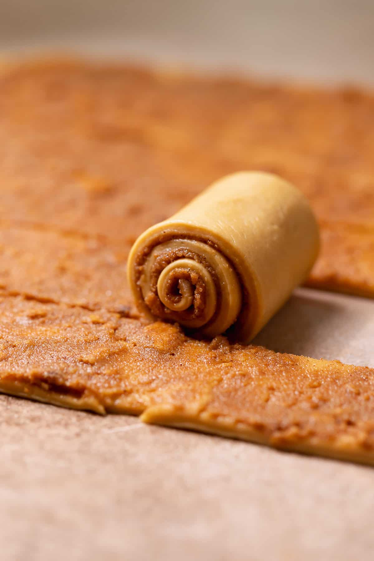 A strip of cinnamon roll dough being rolled up.