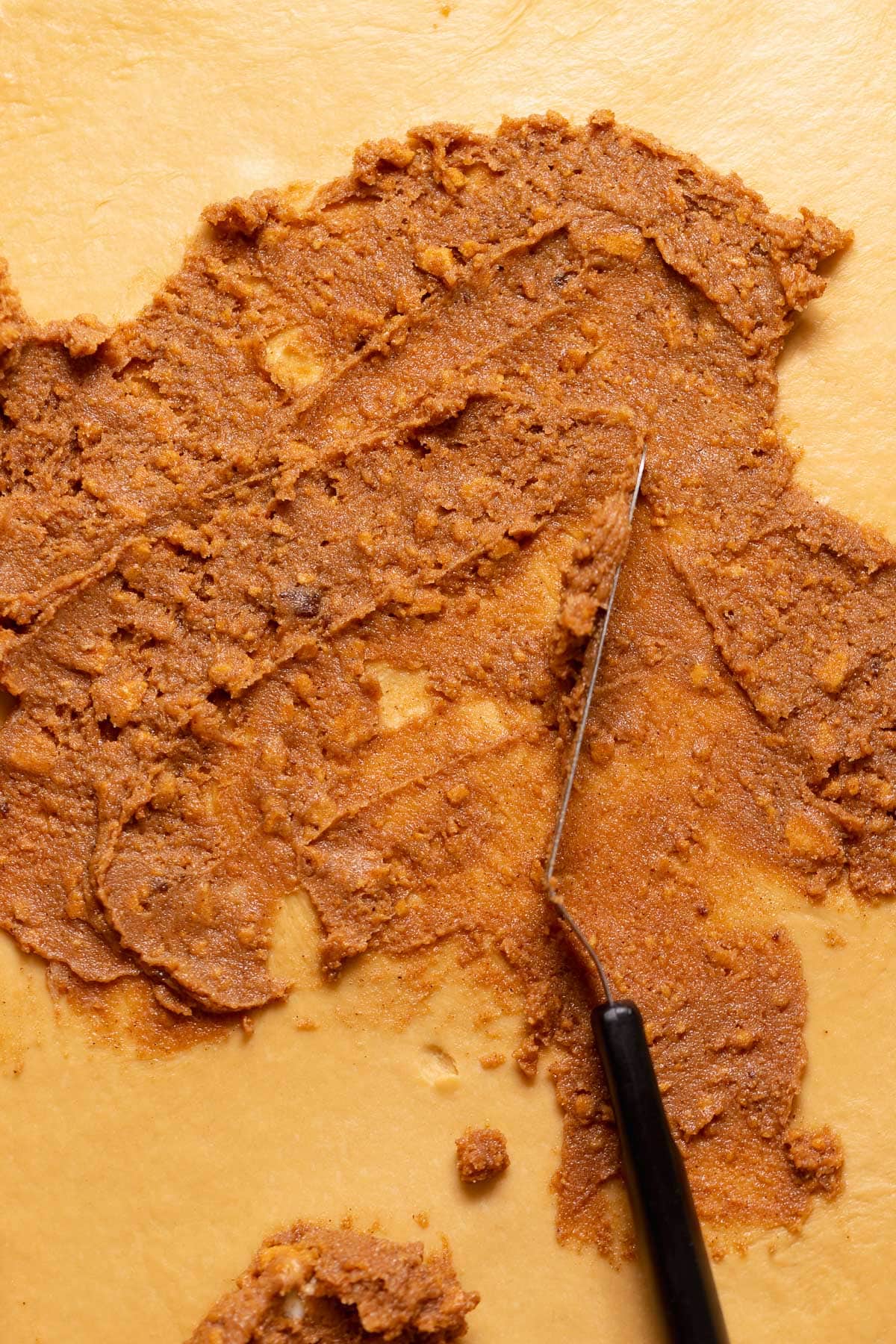 A spatula spreading the spiced gingerbread filling across rolled out dough.