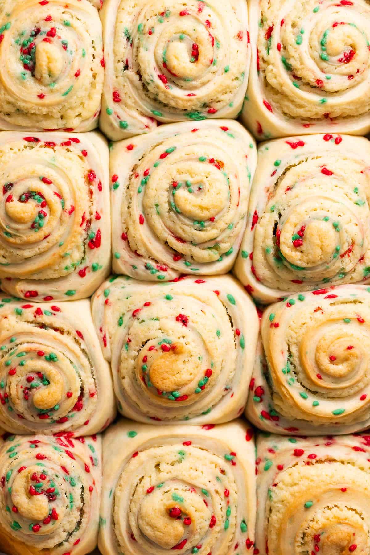 Baked sugar cookie rolls in a pan with visible red and green sprinkles before icing.