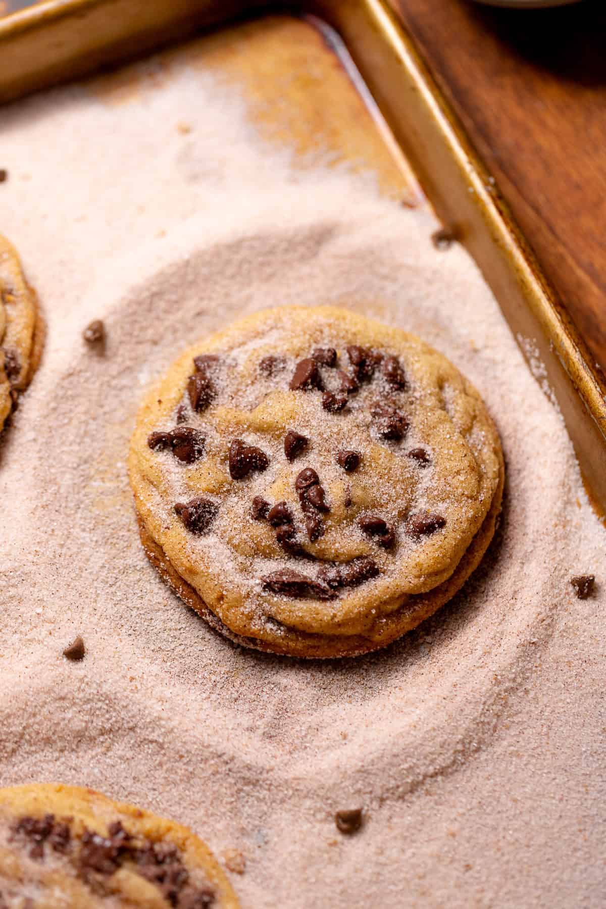 Chocolate chip snickerdoodle cookie coated in cinnamon sugar on a baking sheet