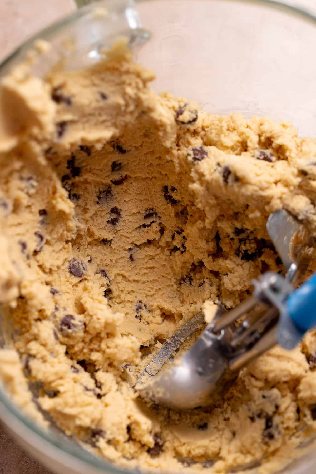 A blue cookie scoop in the mixer bowl with the cookie dough.