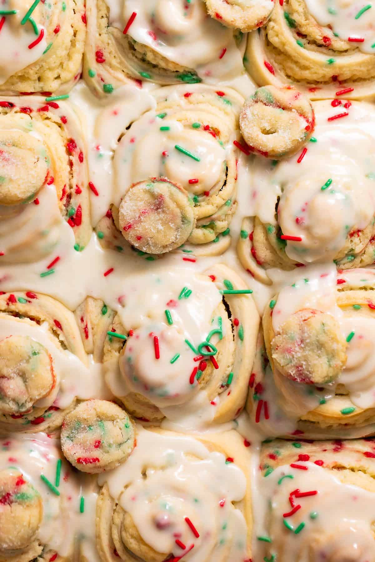 Christmas sugar cookie rolls covered in creamy vanilla icing and holiday sprinkles.