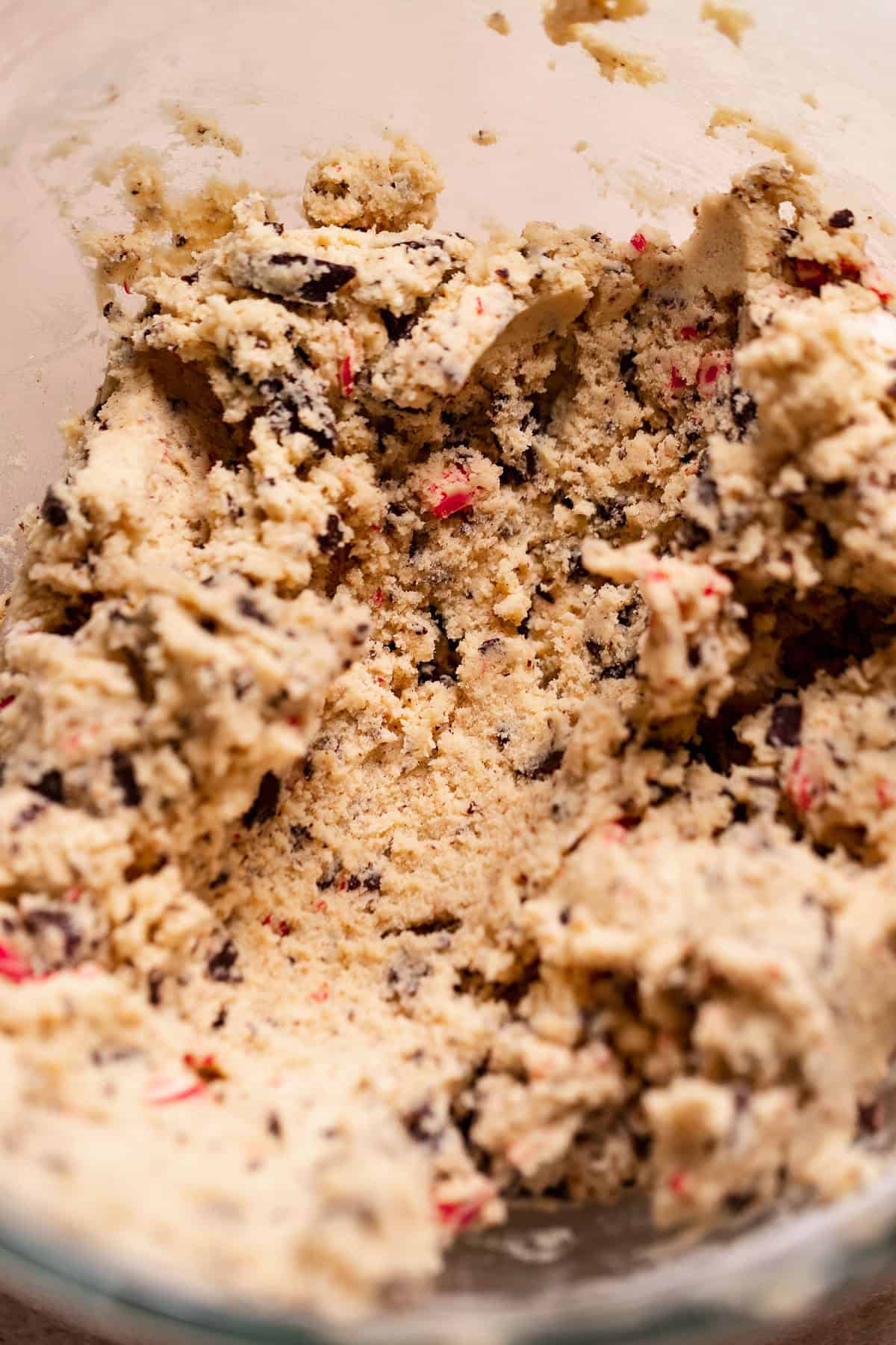 Peppermint chocolate chip cookie dough in a mixing bowl with visible chocolate pieces and crushed candy canes.