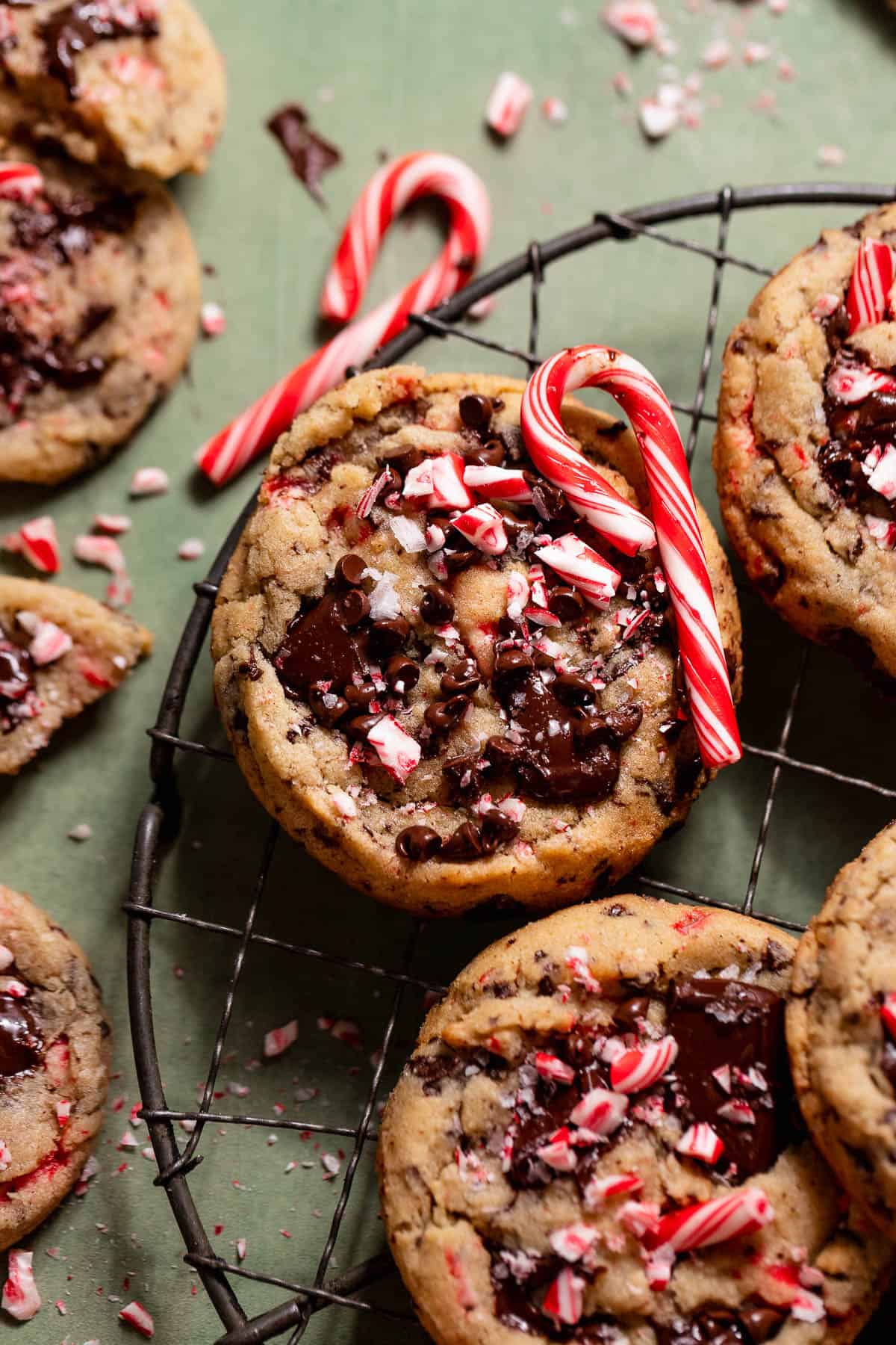 Peppermint chocolate chip cookies topped with chocolate chunks and candy cane pieces on a wire cooling rack.