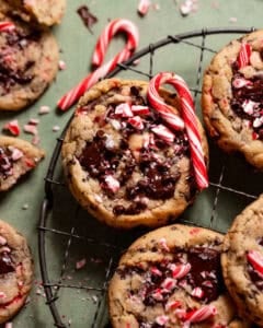 Peppermint chocolate chip cookies topped with melted chocolate and crushed candy canes on a cooling rack.