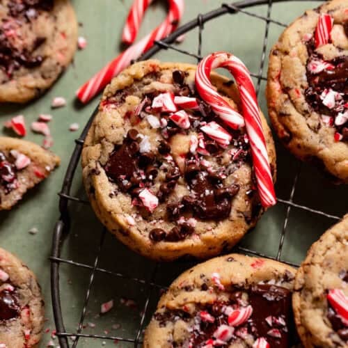 Peppermint chocolate chip cookies topped with melted chocolate and crushed candy canes on a cooling rack.