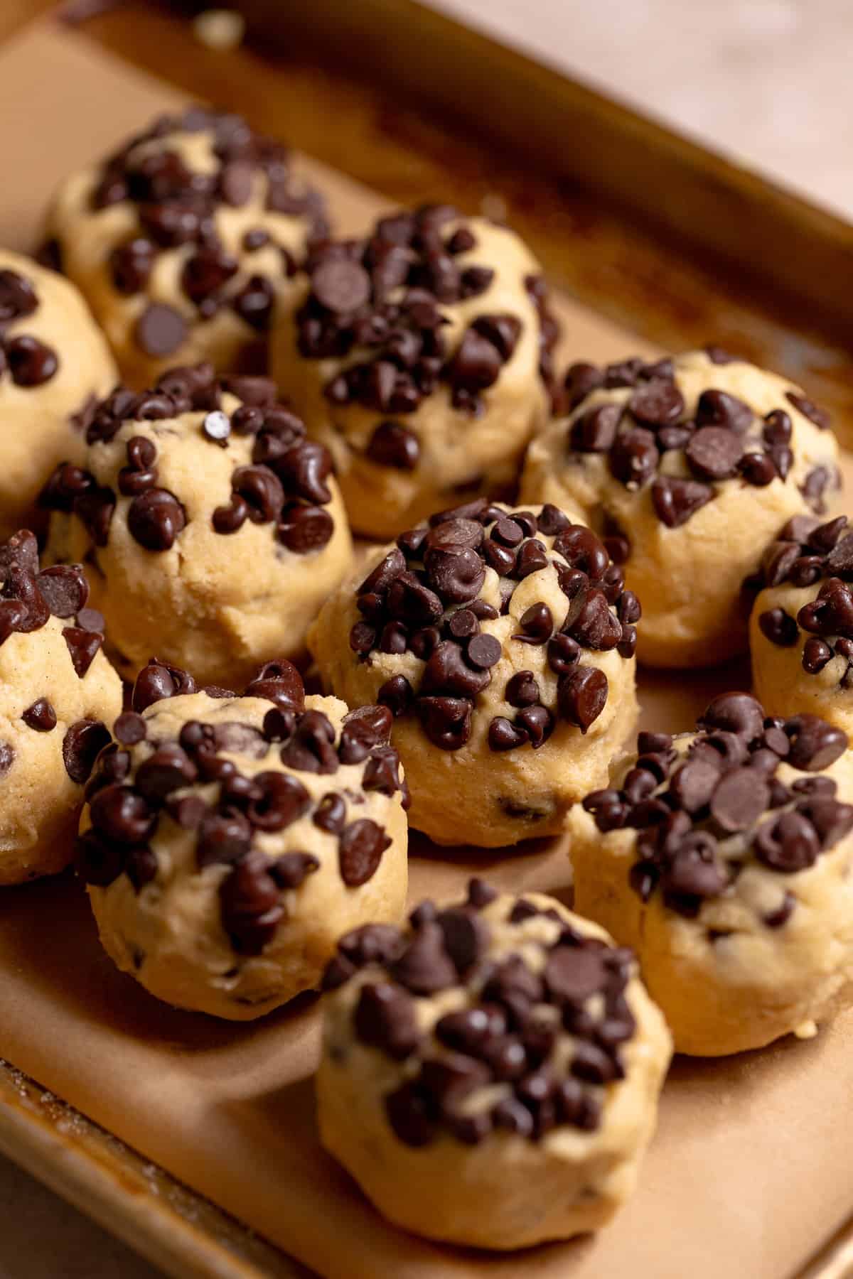 Cookie dough balls with chocolate chips on top on a baking sheet.