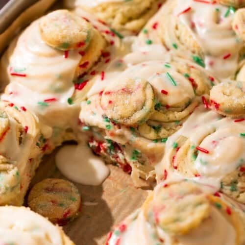 Baked sugar cookie rolls topped with vanilla icing and holiday sprinkles in a pan.