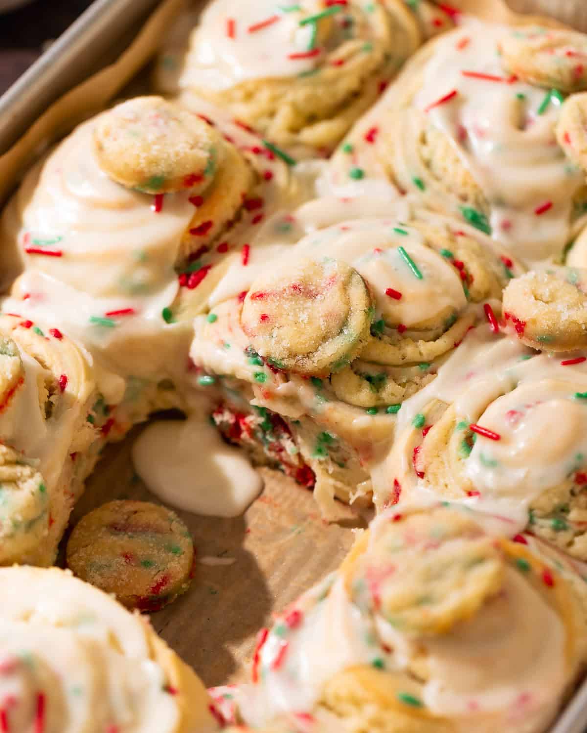 Baked sugar cookie rolls topped with vanilla icing and holiday sprinkles in a pan.
