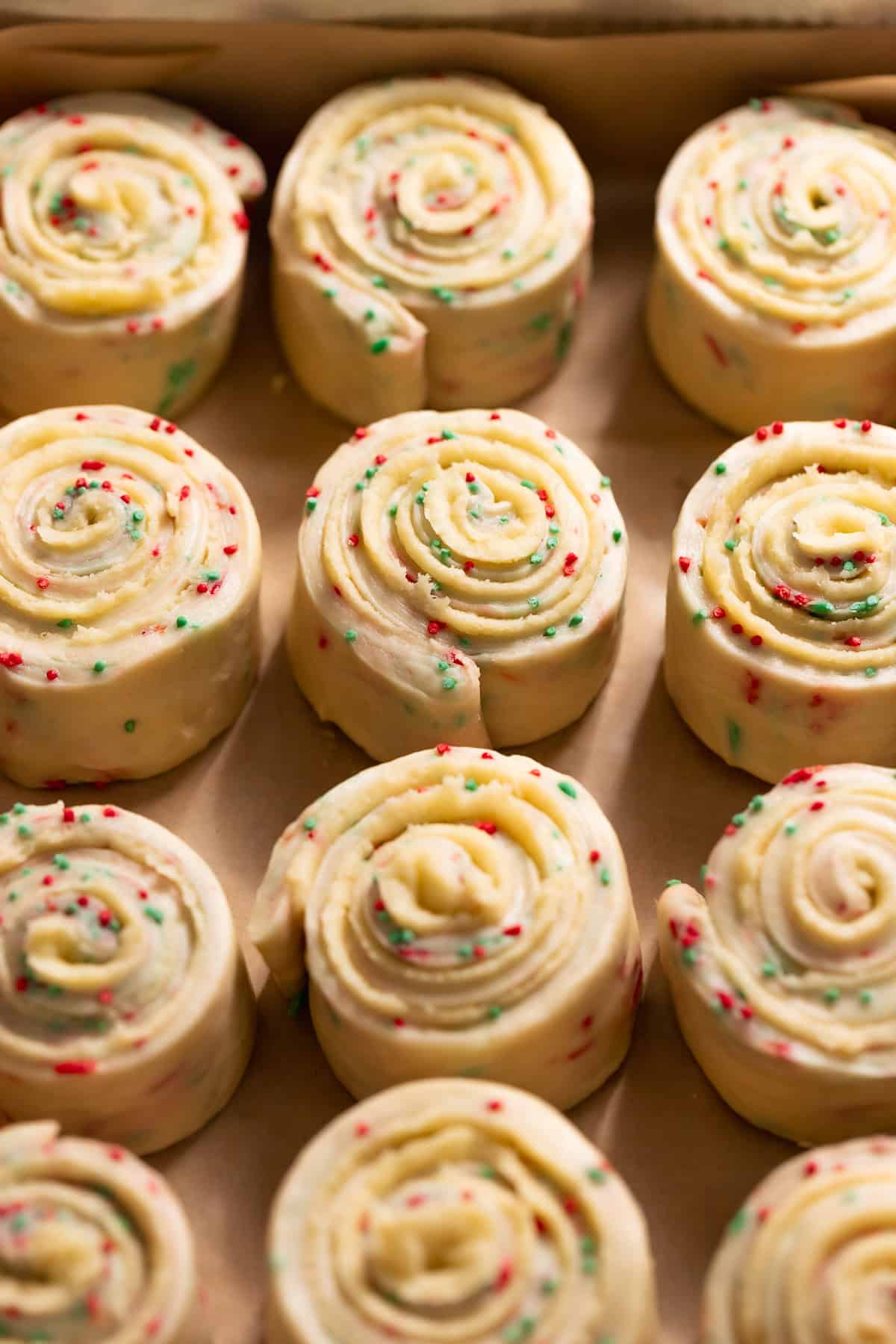 Unbaked sugar cookie rolls with tight spirals and holiday sprinkles in a baking pan.