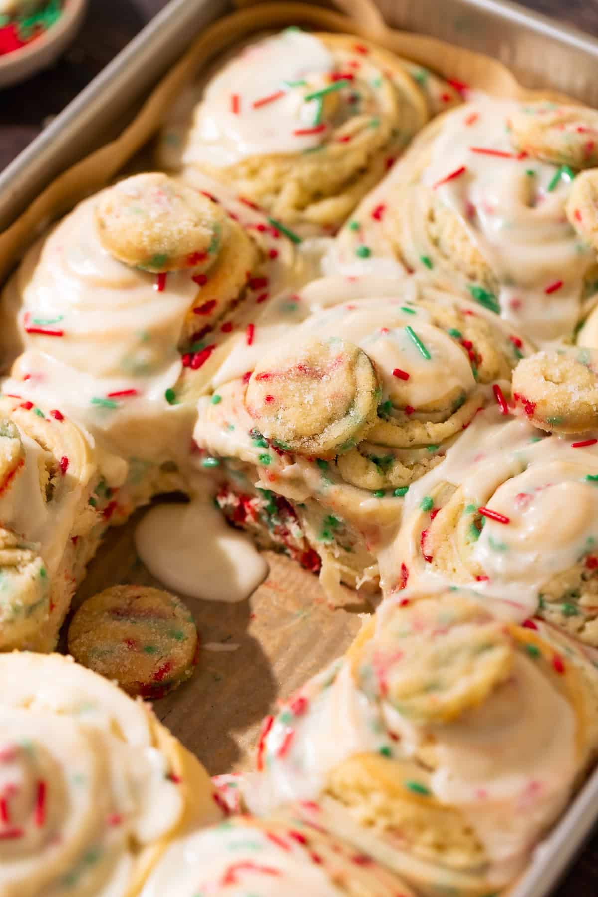 Christmas sugar cookie rolls covered in creamy vanilla icing and holiday sprinkles.