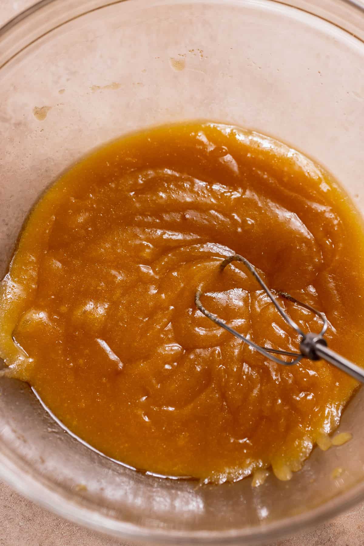 Melted butter and sugar are fully combined in a bowl, creating a thick, golden mixture in a glass bowl.