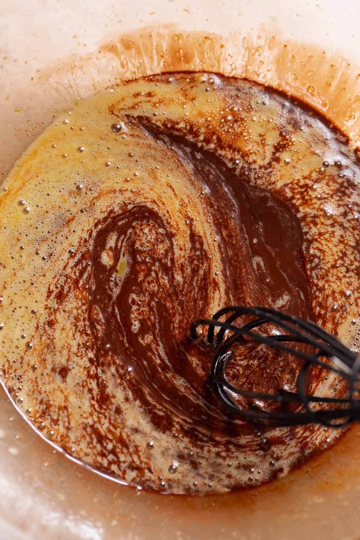 Melted chocolate and eggs being whisked together in a glass bowl.