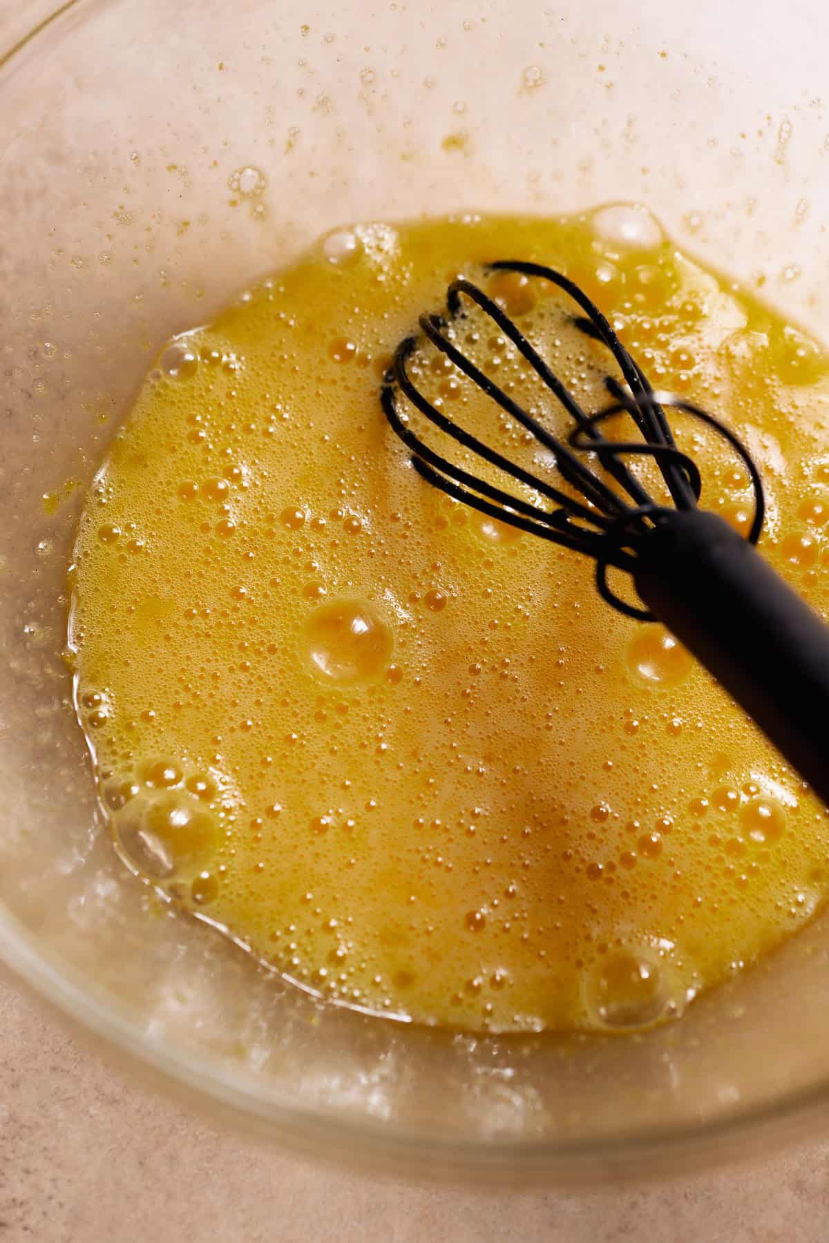 Whisked eggs and sugar in a glass mixing bowl.