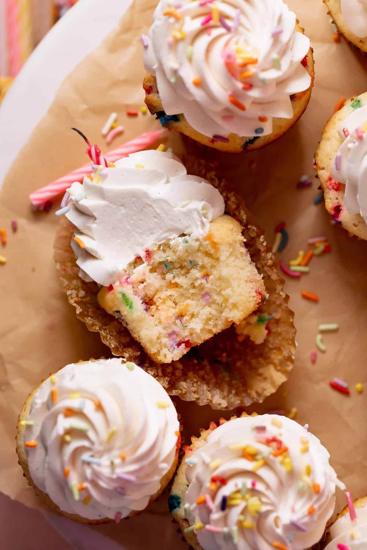 Close-up of a frosted birthday cupcake with a bite taken out, revealing a moist vanilla sprinkle cake crumb and creamy vanilla buttercream.