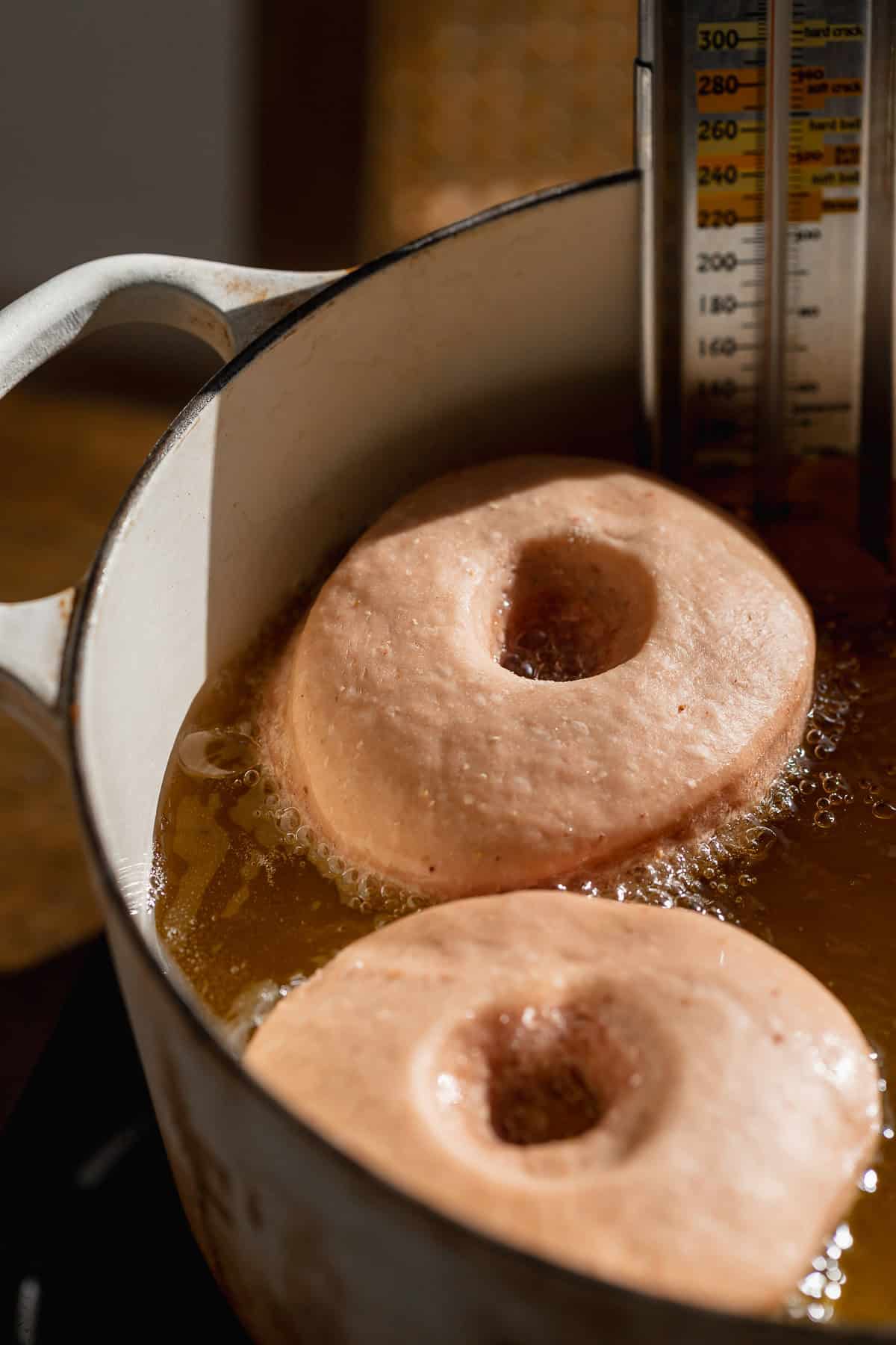 Donuts frying in hot oil in a pot with a thermometer.