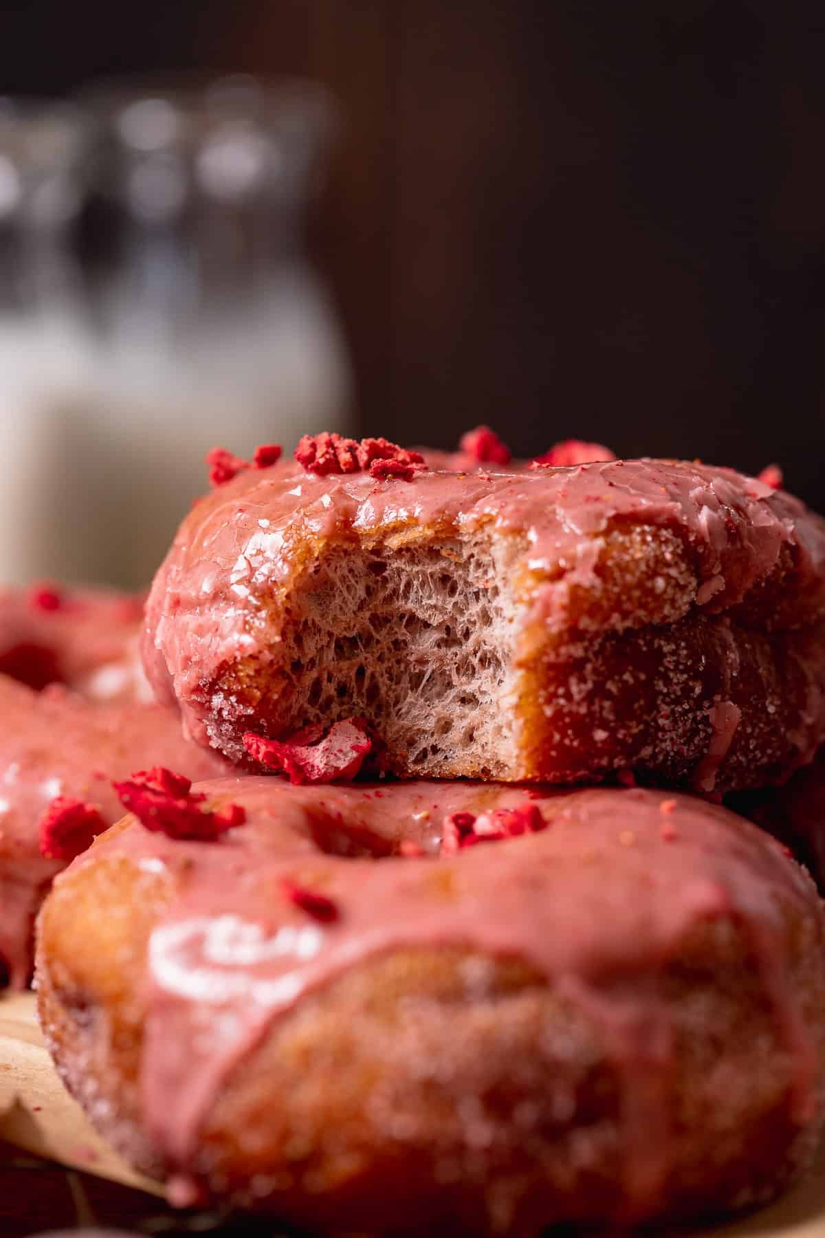Strawberry-glazed donut with a bite taken out, showing the soft, fluffy interior and topped with crushed freeze-dried strawberries.