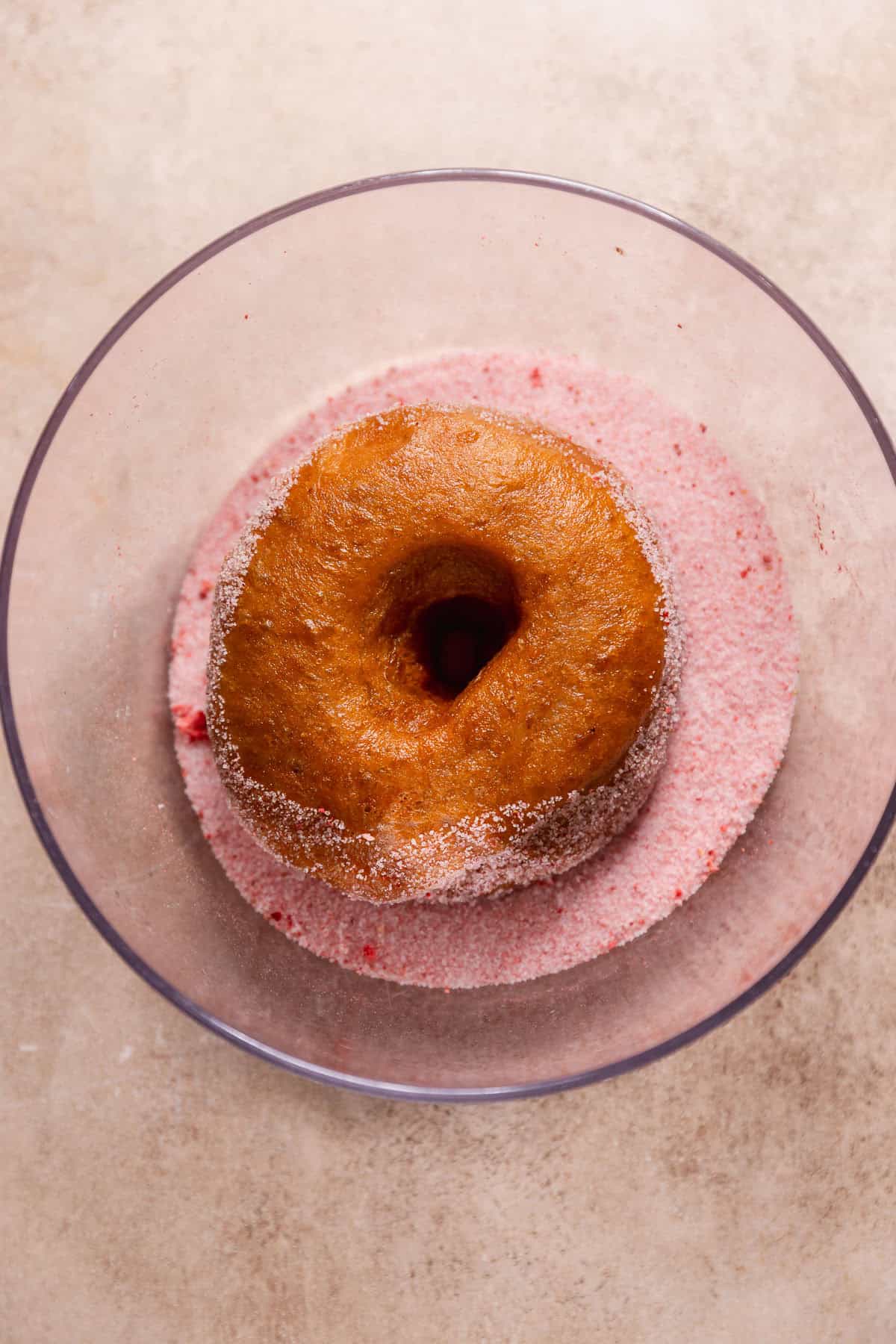 Fried donut coated in strawberry sugar inside a bowl.