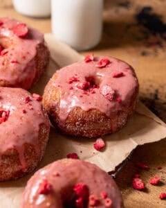 Strawberry-glazed donuts topped with freeze-dried strawberries on a cooling rack with milk in the background.