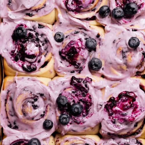 Close-up of blueberry cinnamon rolls with blueberry frosting and fresh blueberries on top.