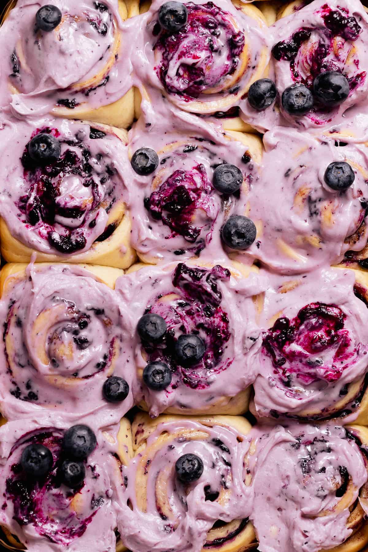 Overhead view of blueberry cinnamon rolls covered in purple blueberry frosting and topped with fresh blueberries.