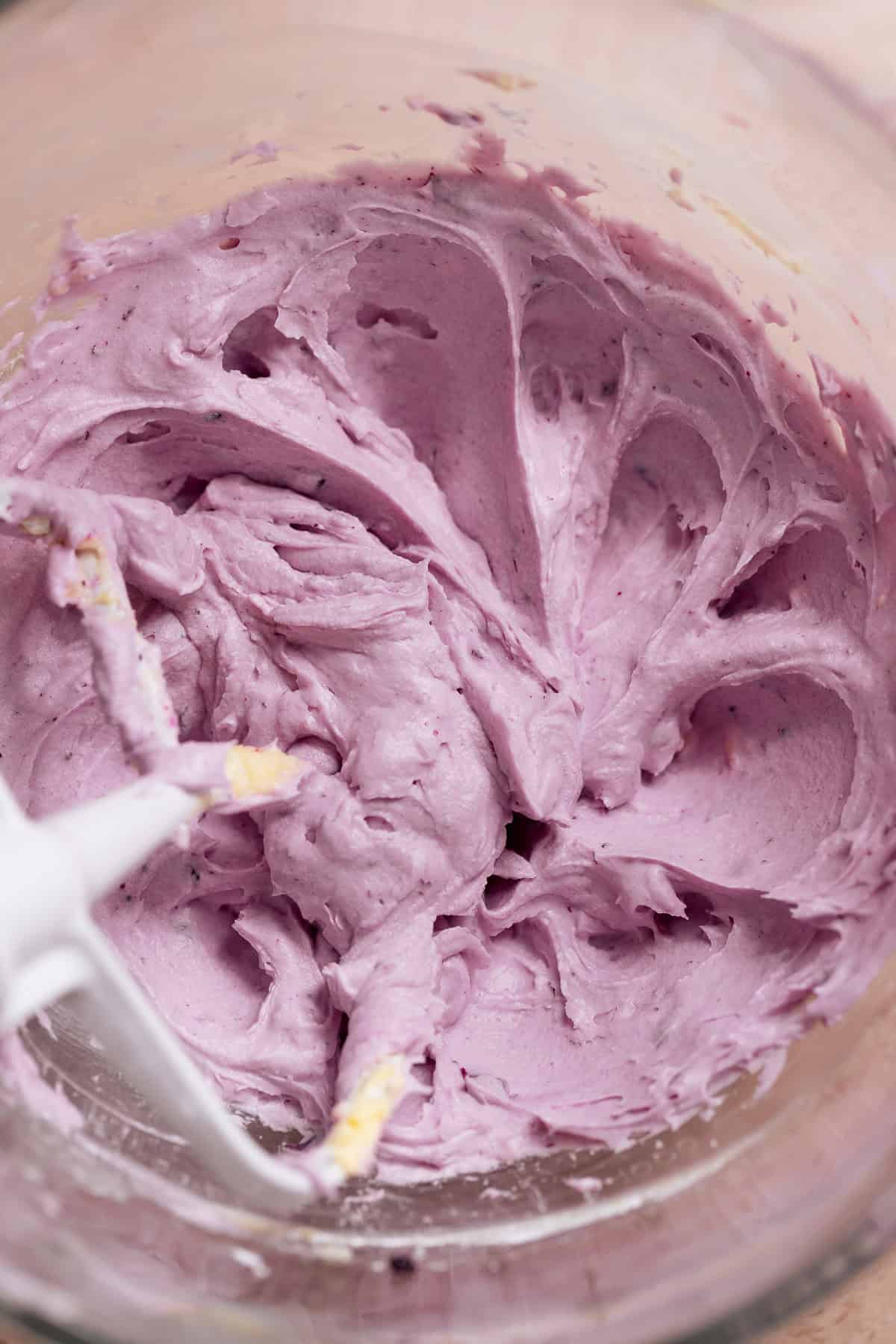 Purple blueberry cream cheese frosting in a mixing bowl with a paddle attachment.