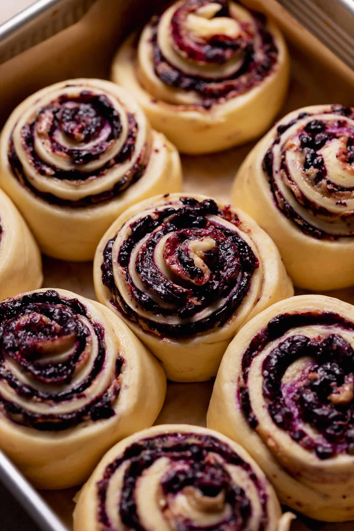 Unbaked blueberry cinnamon rolls with blueberry filling in a parchment-lined baking pan.