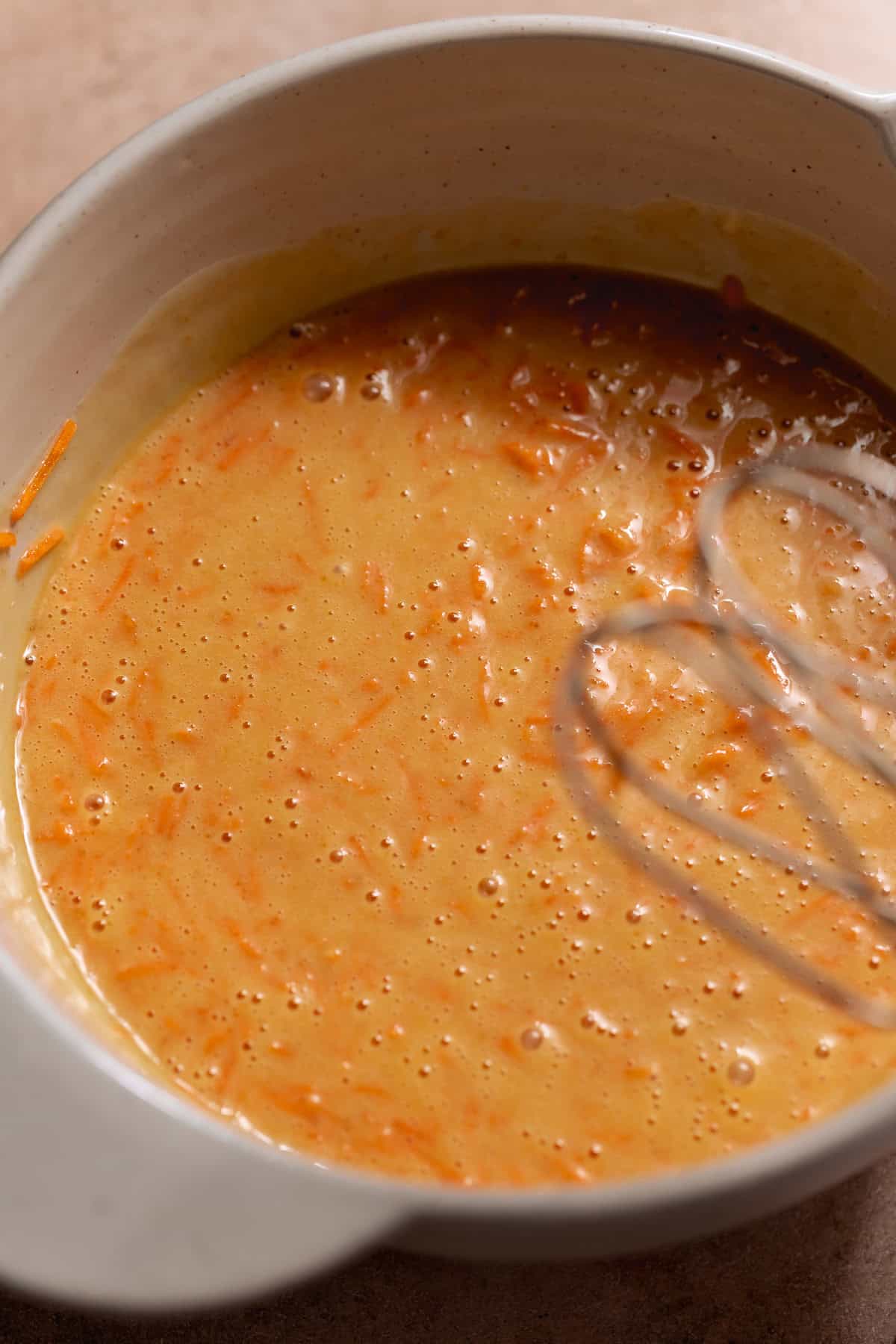 Carrot cake batter with eggs, sugar, oil, and freshly grated carrots being whisked together.