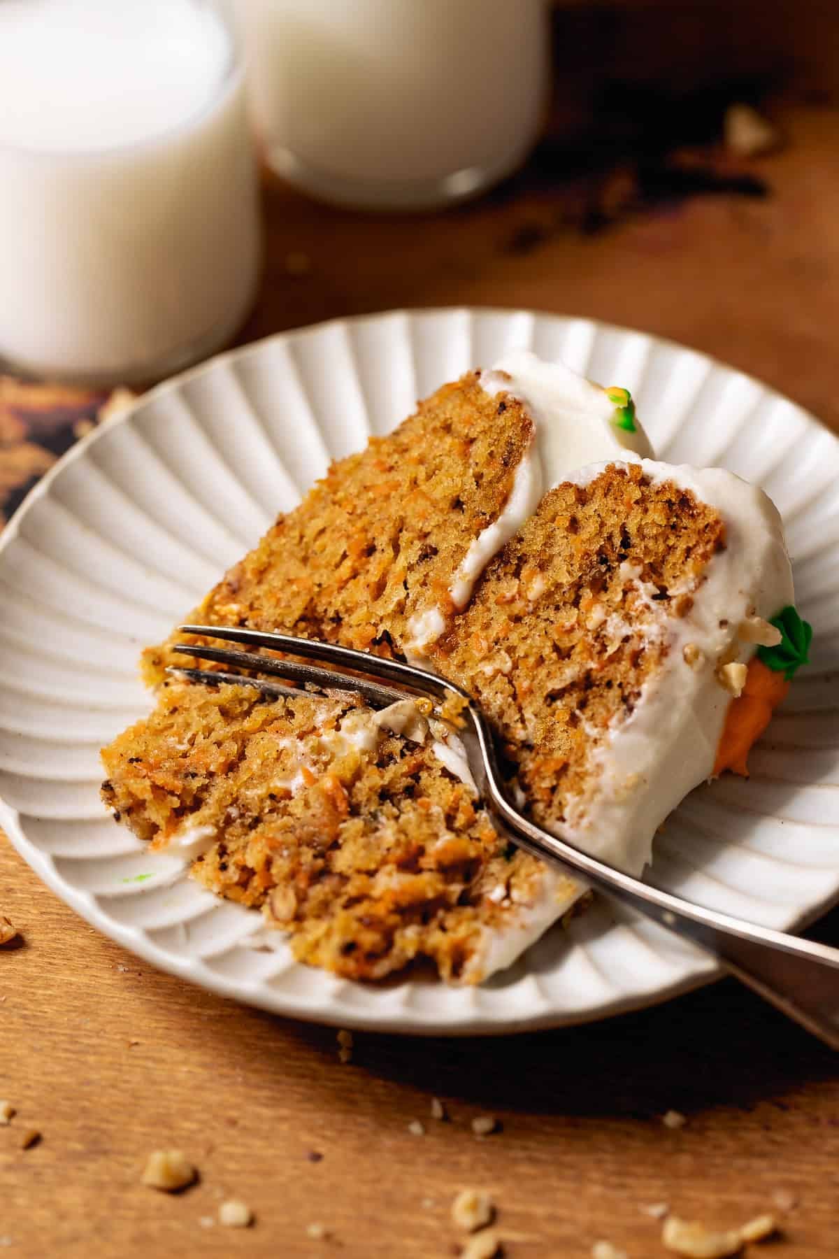 Fork cutting into a slice of carrot cake with cream cheese frosting.