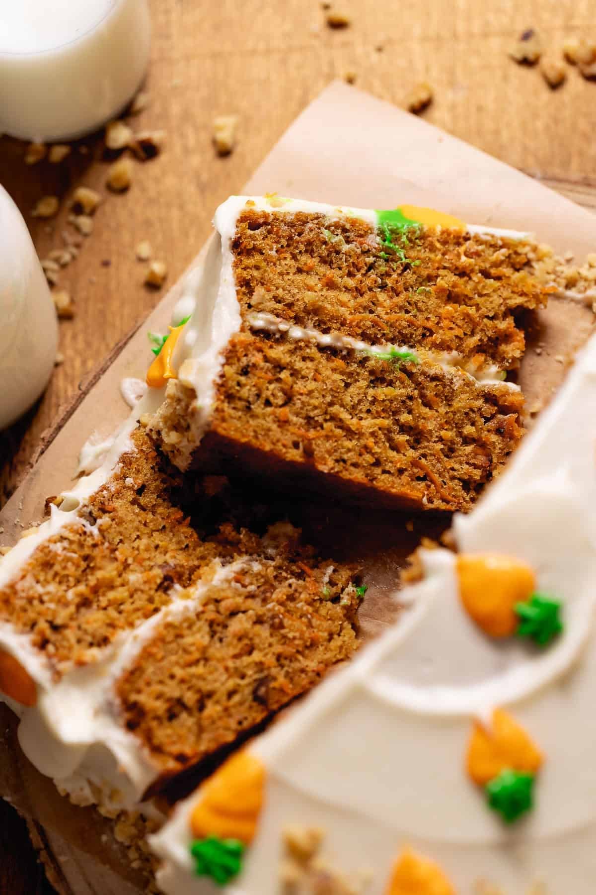 Classic carrot cake with cream cheese frosting and sliced layers on a wooden board.