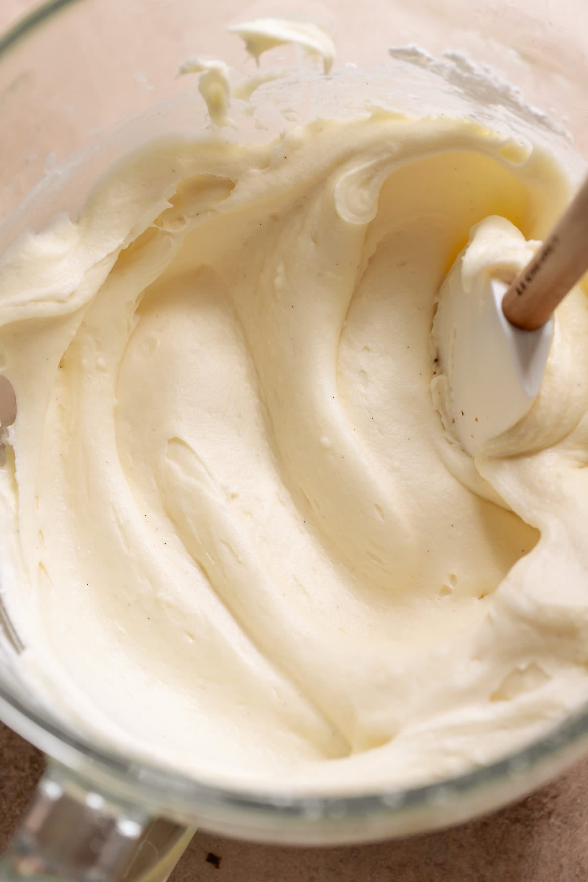 Smooth cream cheese frosting in a mixing bowl with spatula.
