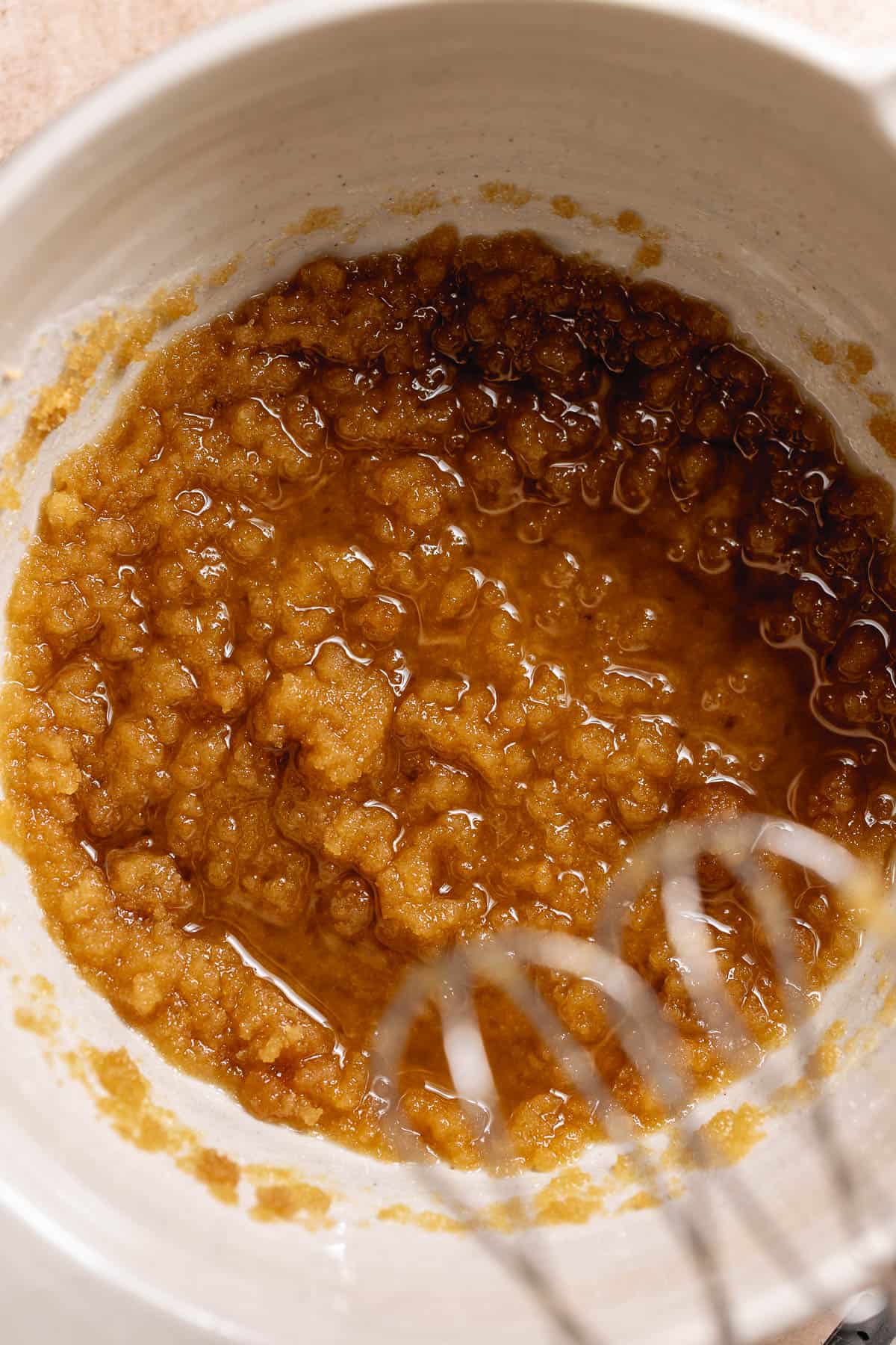 Sugar and oil mixture being whisked in a bowl for carrot cake batter.
