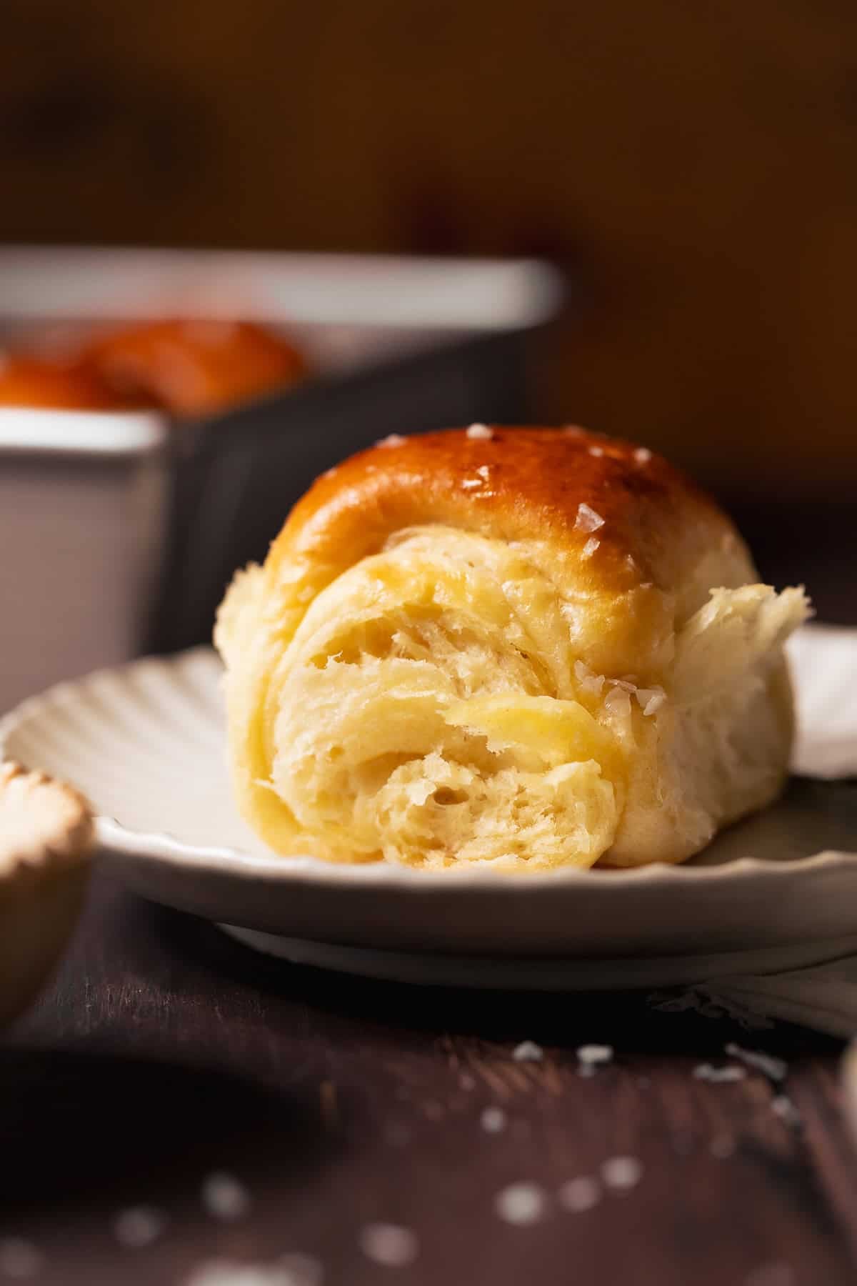 Single homemade dinner roll on a plate with a soft fluffy interior and golden crust.