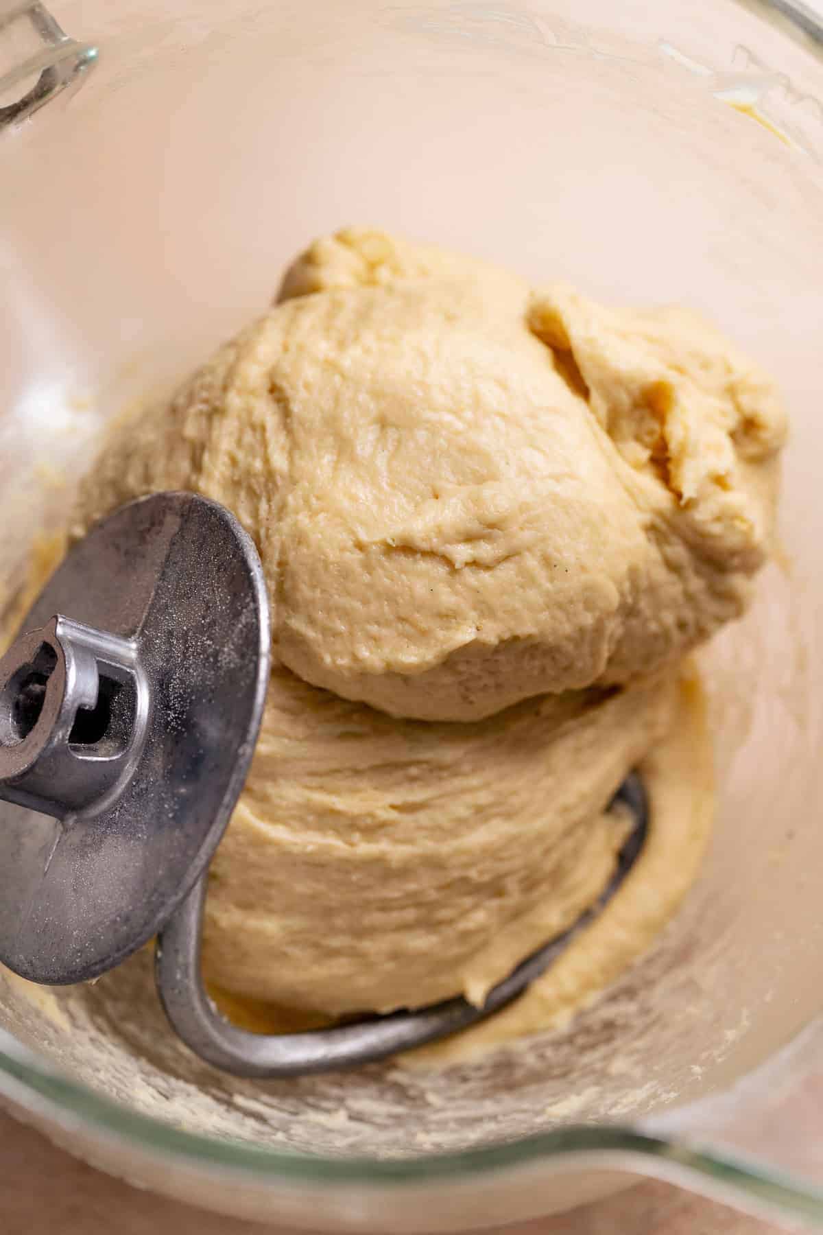 Soft cinnamon roll dough kneading on a dough hook in a stand mixer bowl.