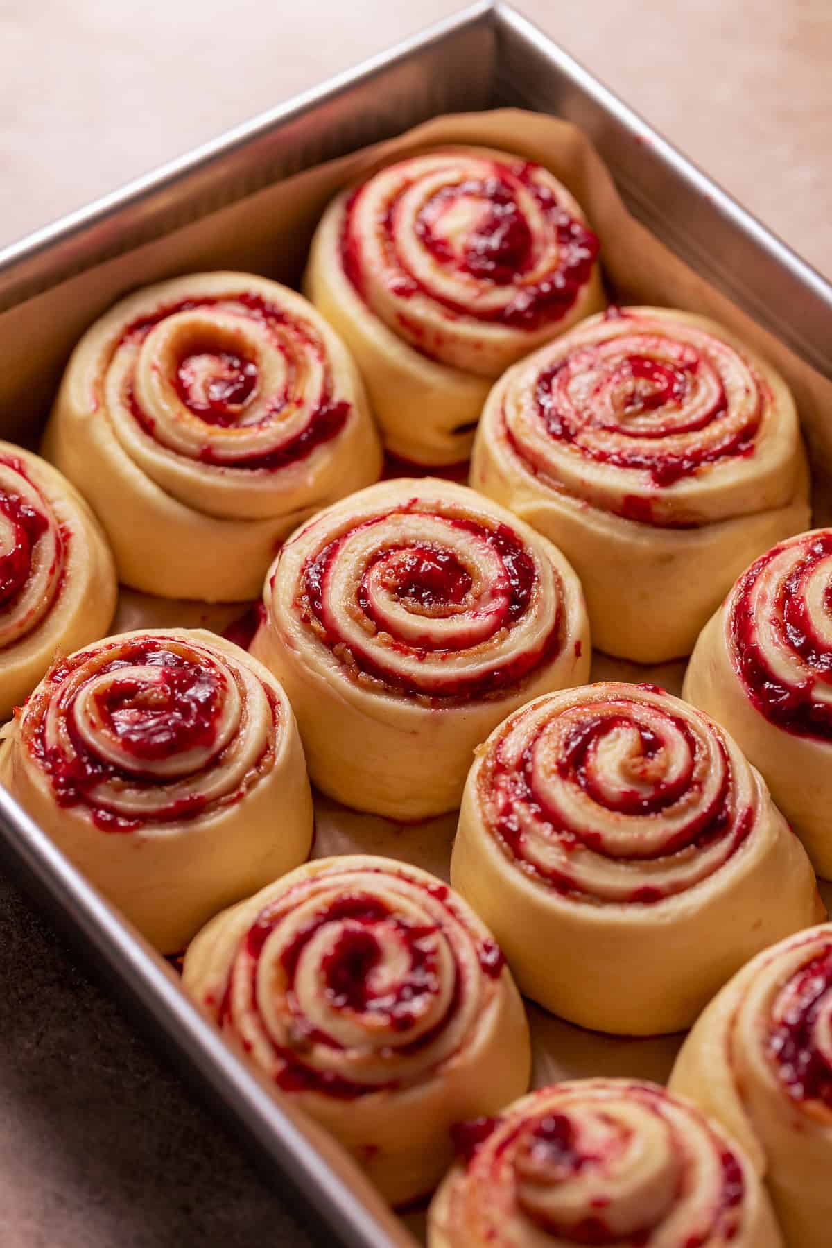 Strawberry cinnamon rolls proofing in a baking pan.