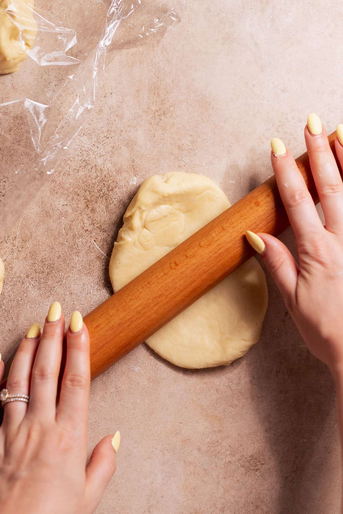 Hands rolling out a portion of dough into a rough rectangle.