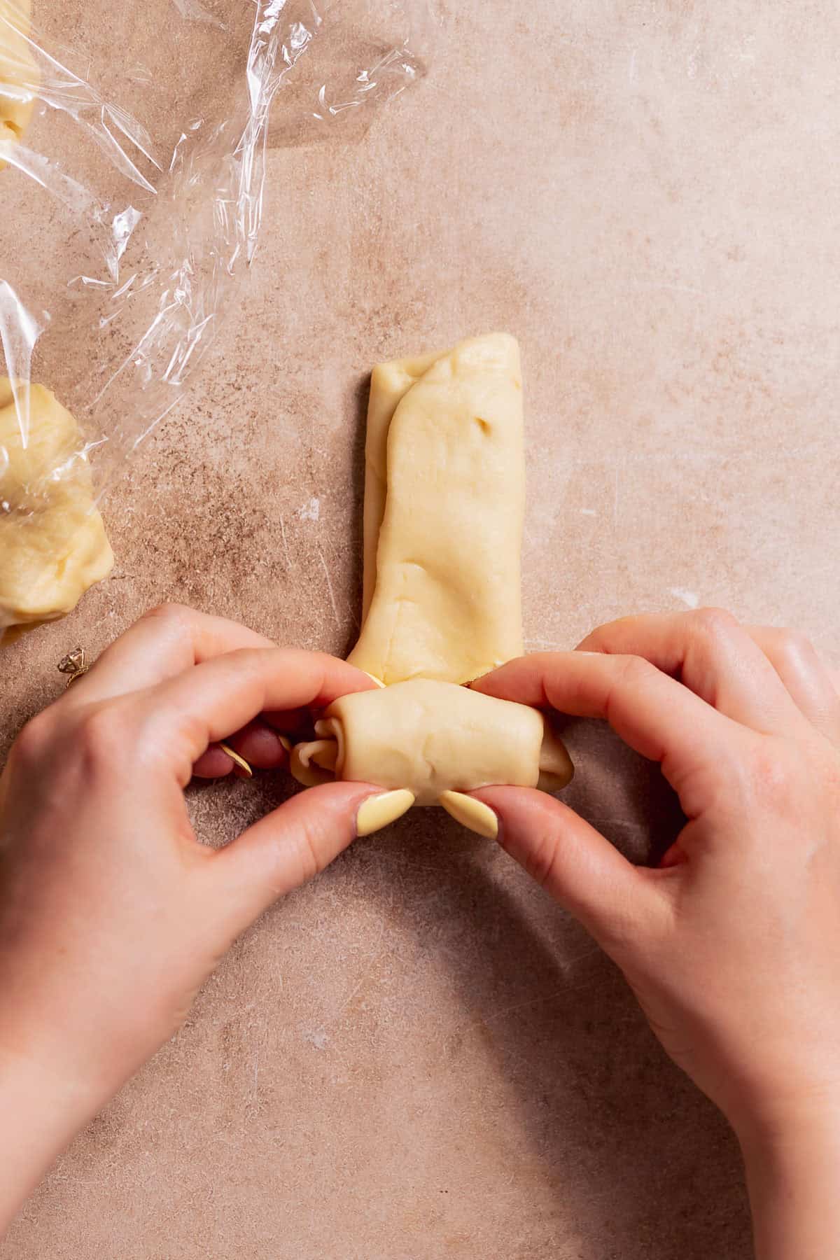 Two hands rolling up the folded dough into a log.