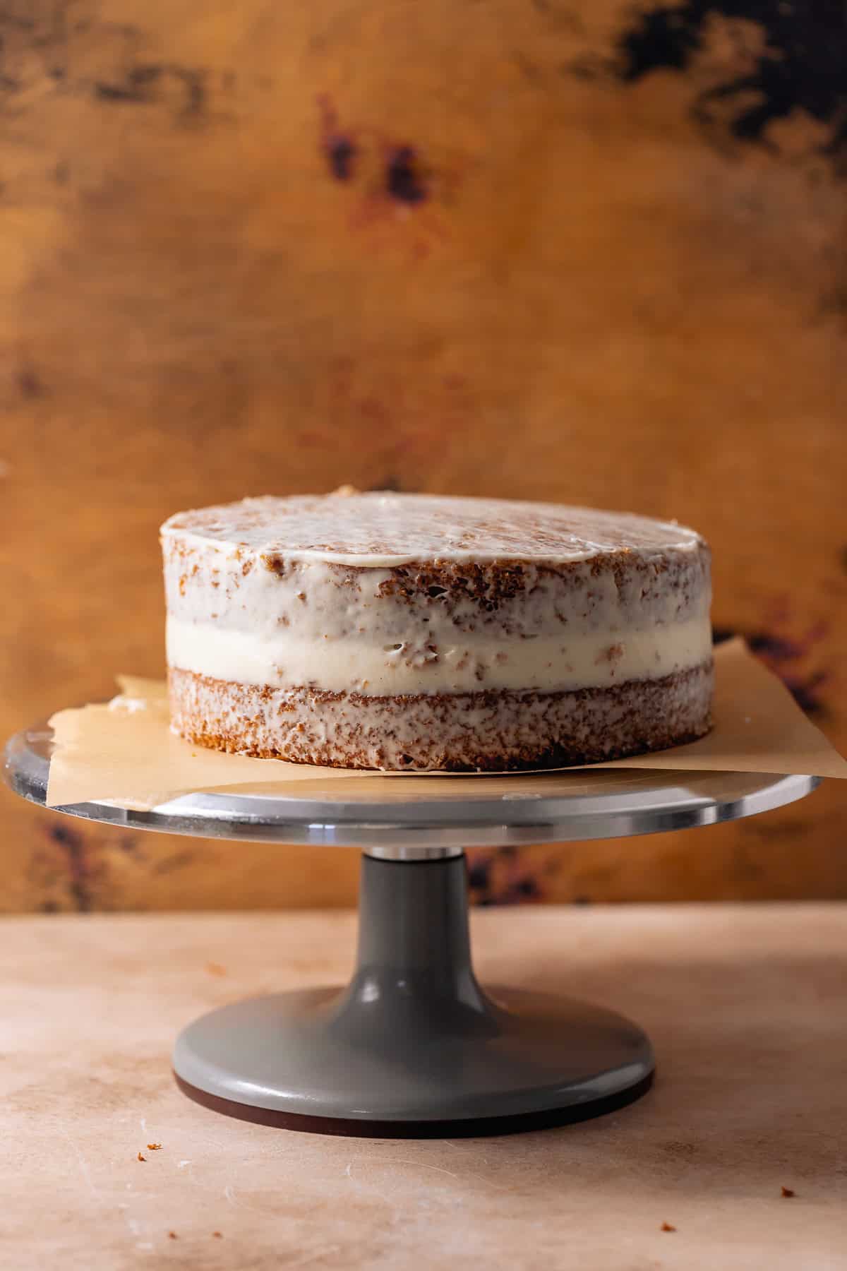 Carrot cake layered and crumb coated with cream cheese frosting on cake stand.