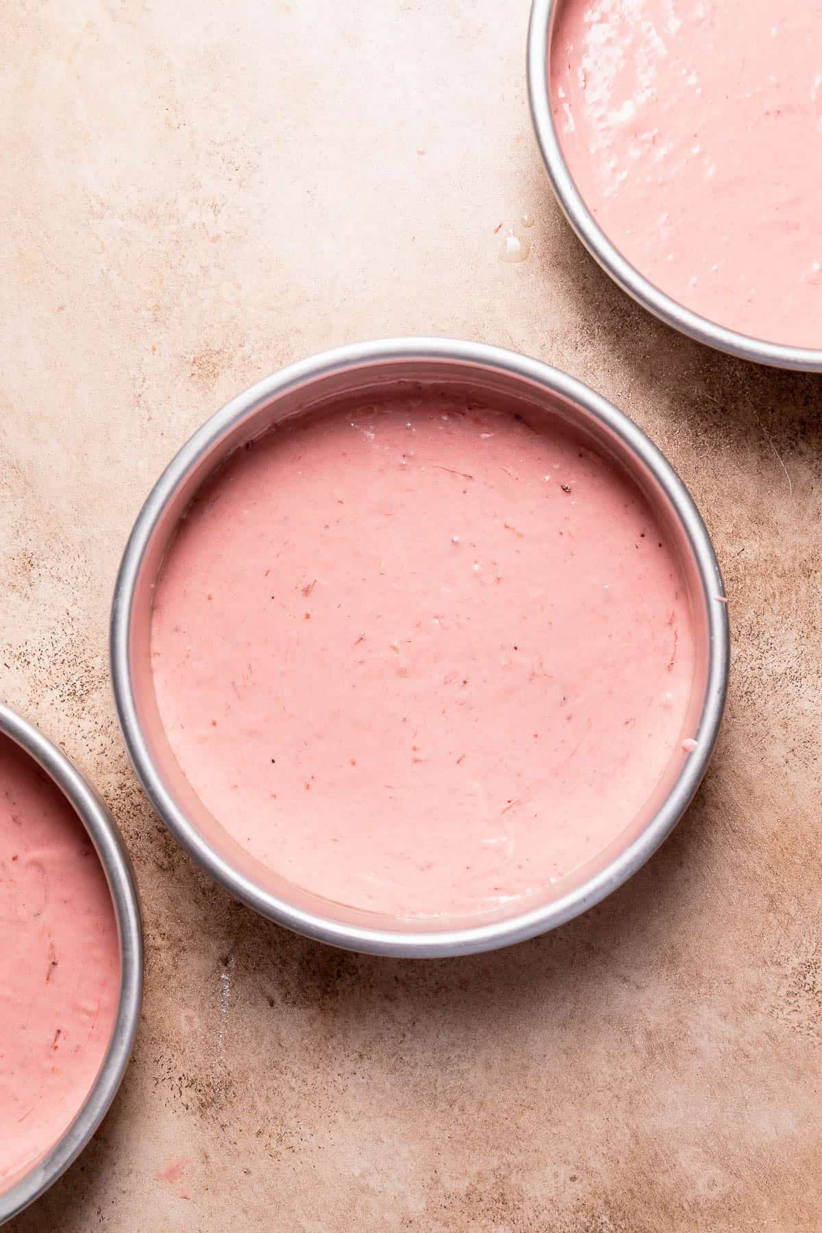 Strawberry cake batter divided into round cake pans before baking.