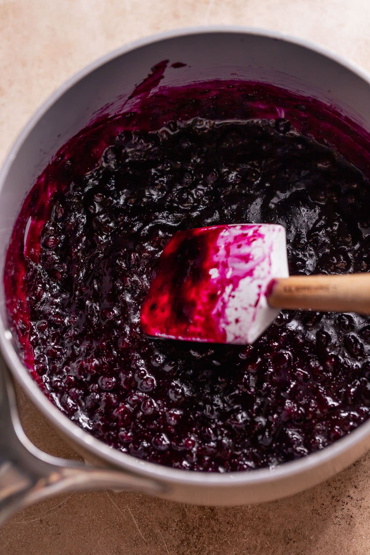 Saucepan of thick wild blueberry jam with a spatula stirring.