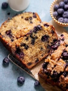 Slices of blueberry banana bread on parchment paper with fresh blueberries nearby.