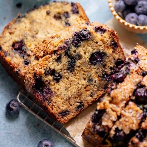 Slices of blueberry banana bread on parchment paper with fresh blueberries nearby.