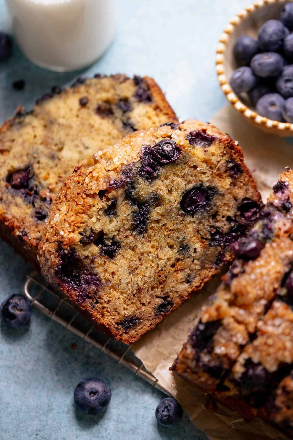 Sliced blueberry banana bread served with a glass of milk and fresh blueberries.