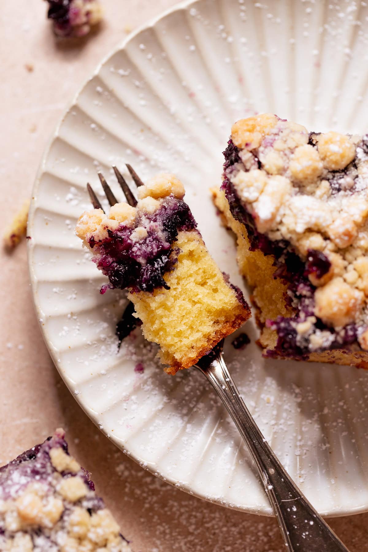 Forkful of blueberry cake with crumb topping on a white plate.