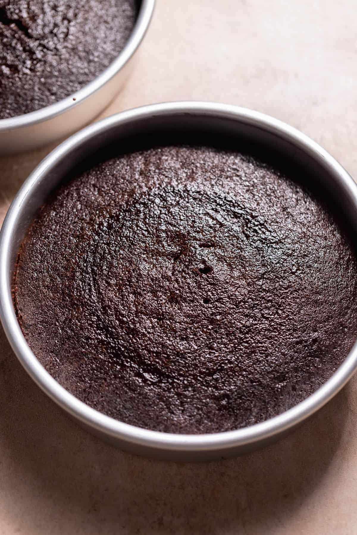 Two round chocolate cake layers baked in metal pans with a smooth, even surface.
