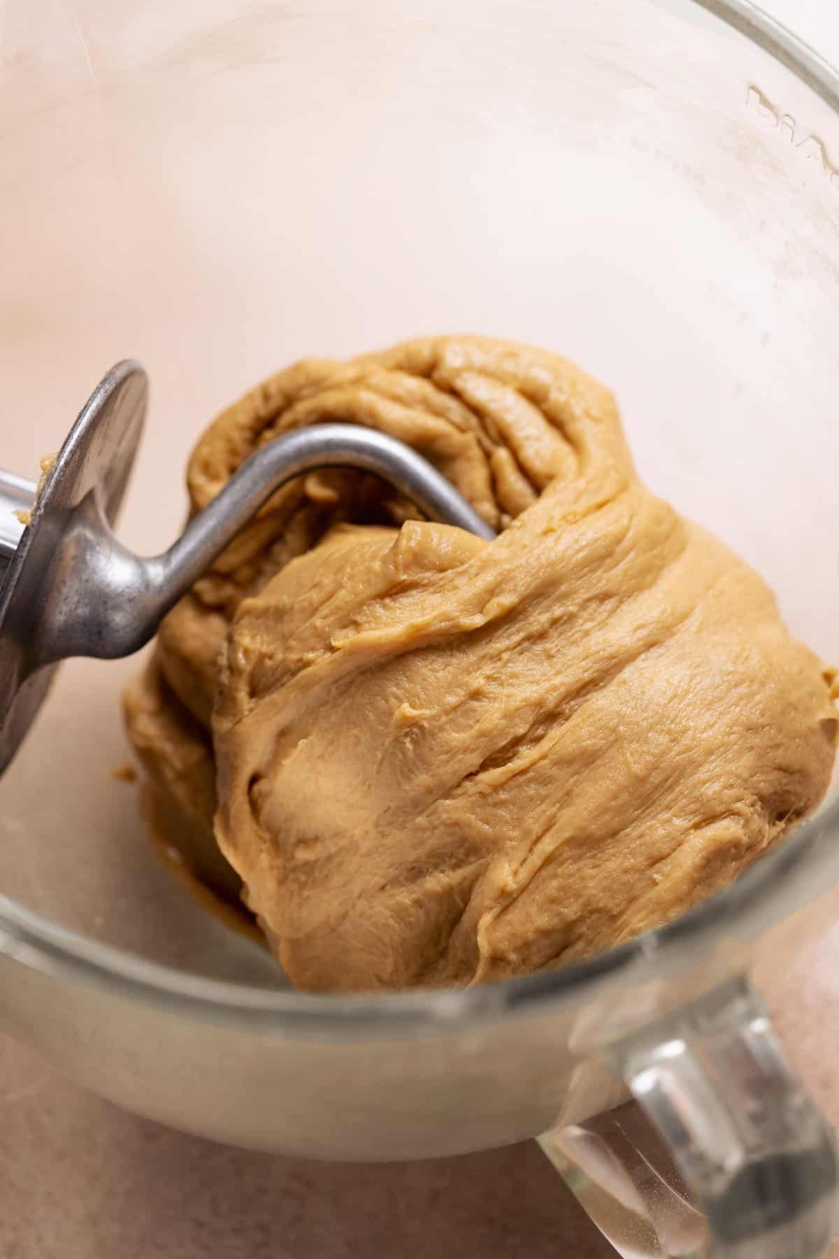 Soft enriched cinnamon roll dough with coffee flavor being kneaded in a stand mixer with a dough hook.